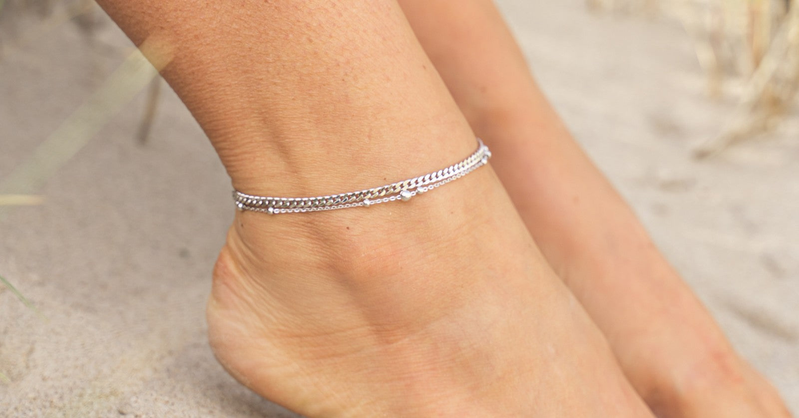 Ankel med 2 tynde sølv ankelkæder på. Et med flad kæde og den anden med små kugler fordelt på kæden